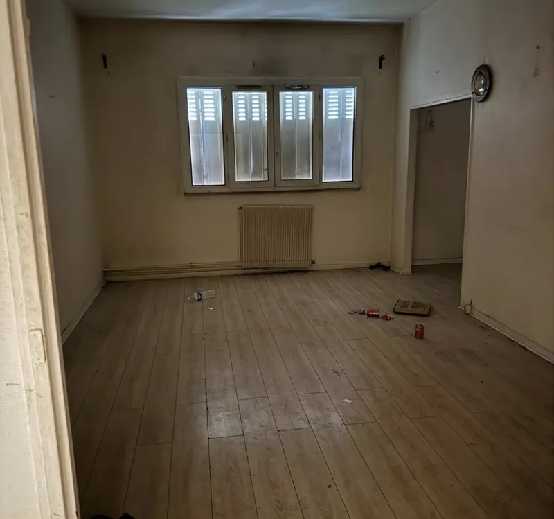 Grande pièce avant travaux : ancien parquet, murs encrassés, gravats au sol