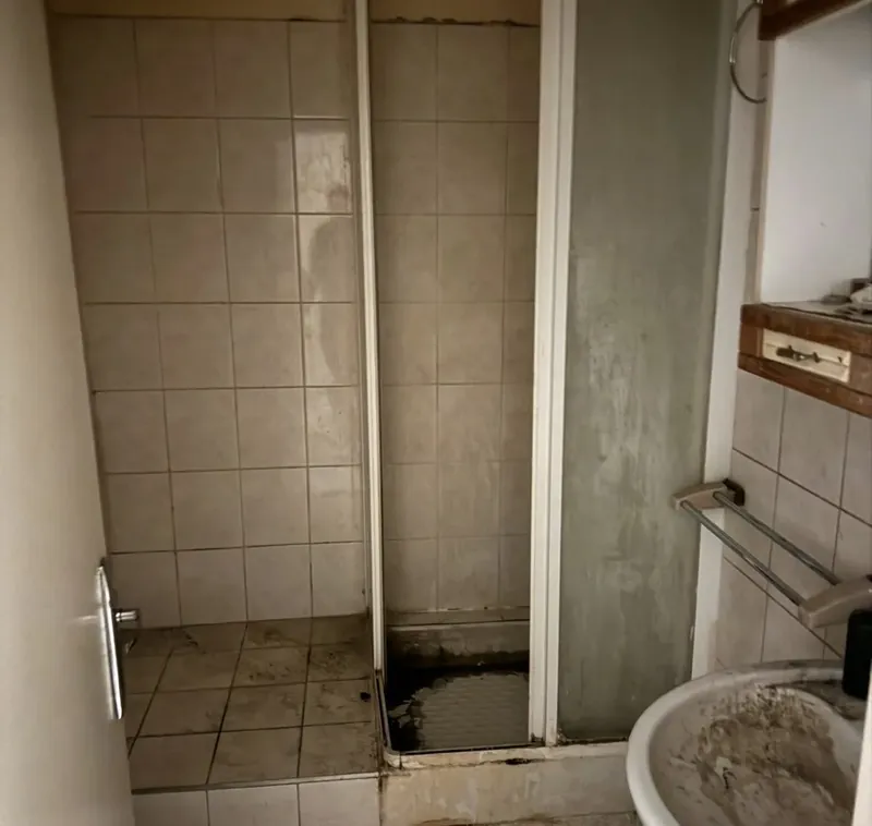 Ancienne salle d'eau : douche carrelée encrassée, lavabo et faïence d'origine