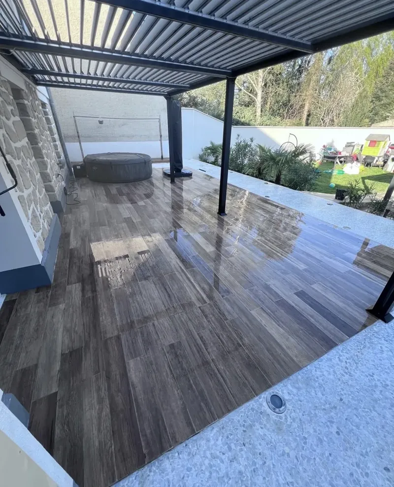 La pergola bioclimatique et ses lames orientables, au-dessus du carrelage extérieur bordé de béton désactivé